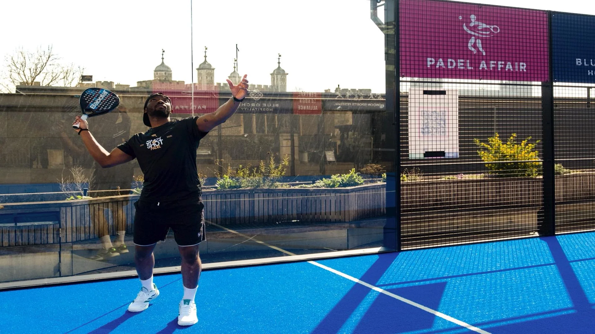 Lemzi mid-serve on an outdoor padel court
